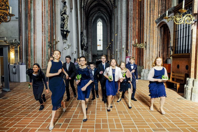 Junge Menschen laufen fröhlich in festlicher Kleidung durch eine Kirche. - Copyright: Thorsten Wulff